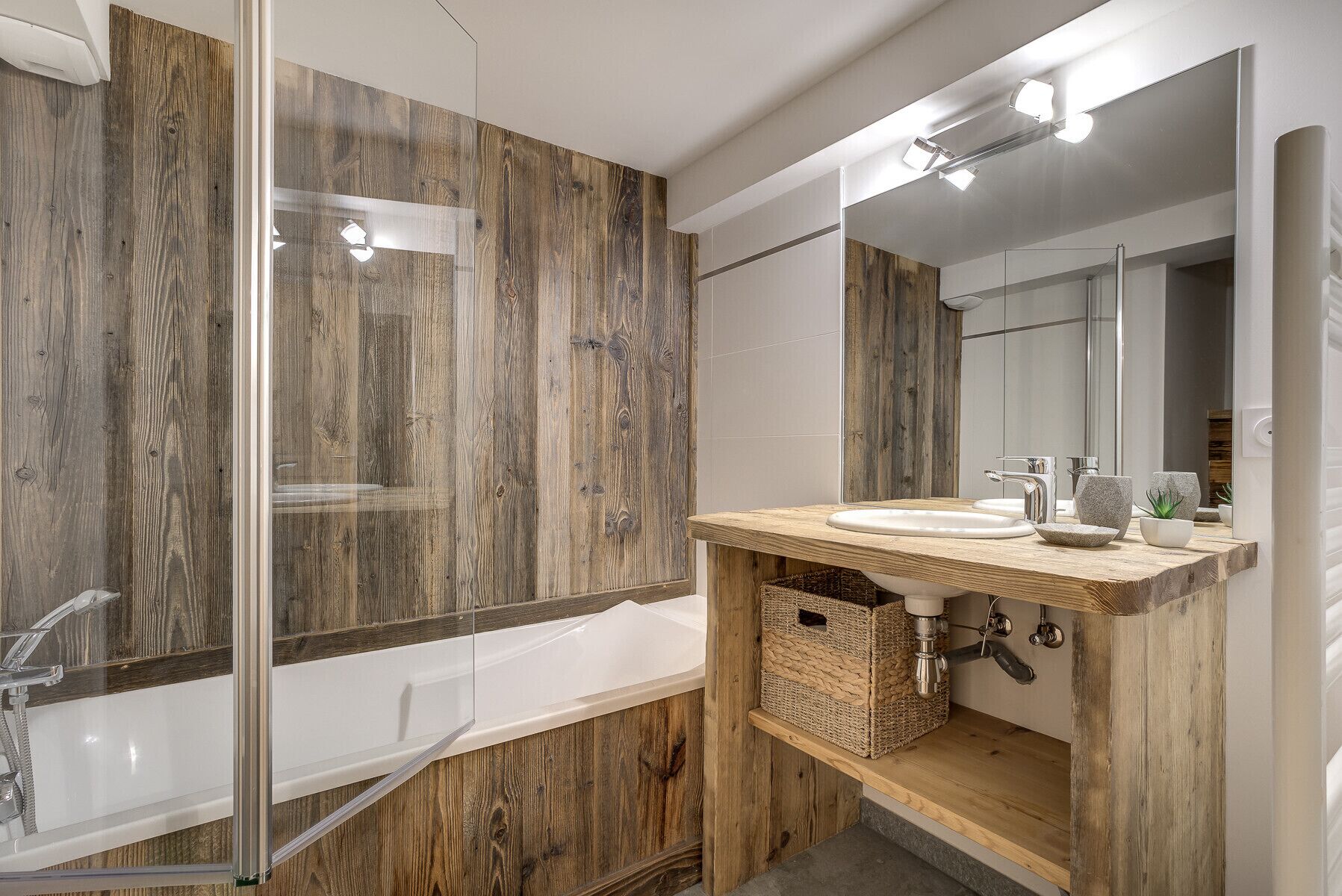 A modern bathroom with a wooden vanity, a large mirror, and a bathtub.