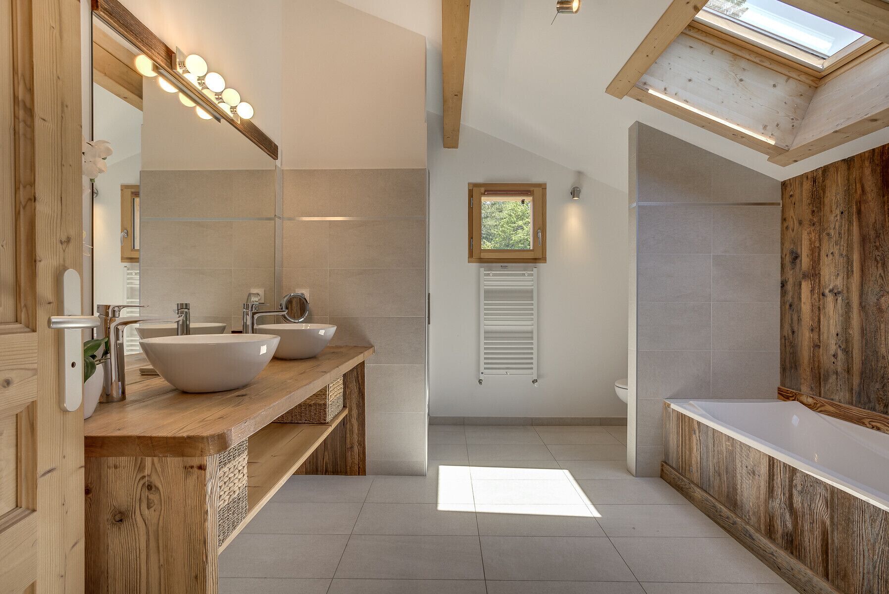 A modern bathroom with two sinks, a large mirror, and a skylight.