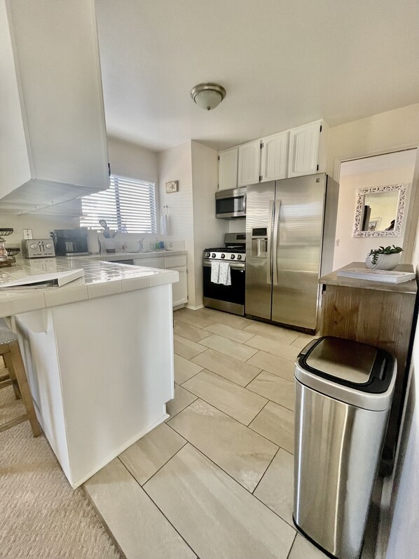 A modern kitchen with white cabinetry, stainless steel appliances, and a tiled floor.