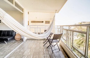 A balcony with a white hammock, a black sofa, and wicker chairs.