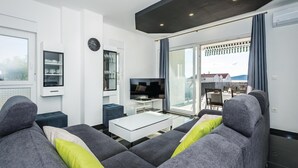 A modern living room with grey sofas, a coffee table, a TV, and a dining area with a table and chairs. - Beach front home in Brodarica with house sea view (Brodarica)