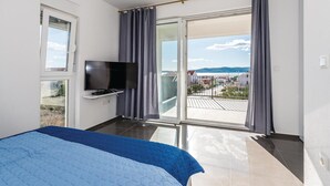A hotel room with a bed, a TV mounted on the wall, and a balcony with a view of the sea and buildings. - Beach front home in Brodarica with house sea view (Brodarica)