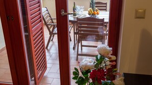 Puerta abierta a un comedor con una mesa dispuesta para dos personas, un frutero y un jarrón de flores.