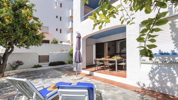 Un patio con dos sillones blancos, una mesa y una sombrilla.