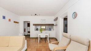 Un espacio habitable compacto con kitchenette, comedor y dos sofás color beige.