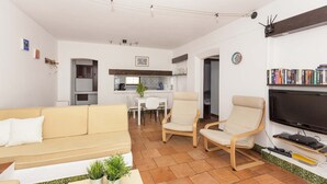 Una sala de estar con sofá, sillas, televisor y estantería.