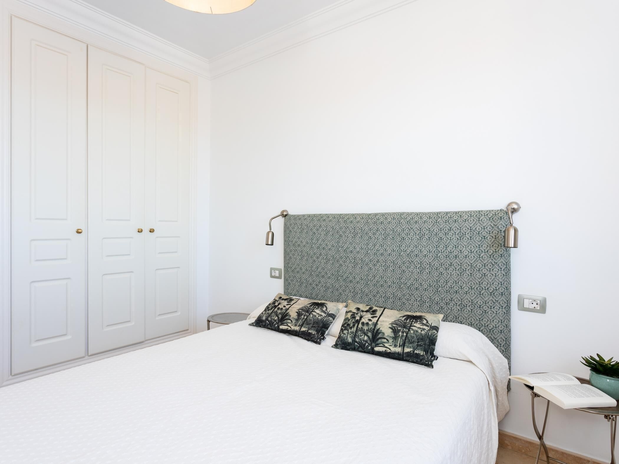 Een slaapkamer met een bed, nachtkastje, lamp en kledingkast.