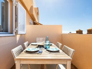 A wooden table set for two with white plates and blue glassware, surrounded by wicker chairs, against a beige wall with a window and shutters. - Nice terrace apartment, shared pool - PORÍS 2 (Porís de Abona)