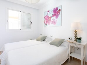 A bedroom with two beds, a bedside table with a lamp, a potted plant, and a wall-mounted picture. - Nice terrace apartment, shared pool - PORÍS 2 (Porís de Abona)