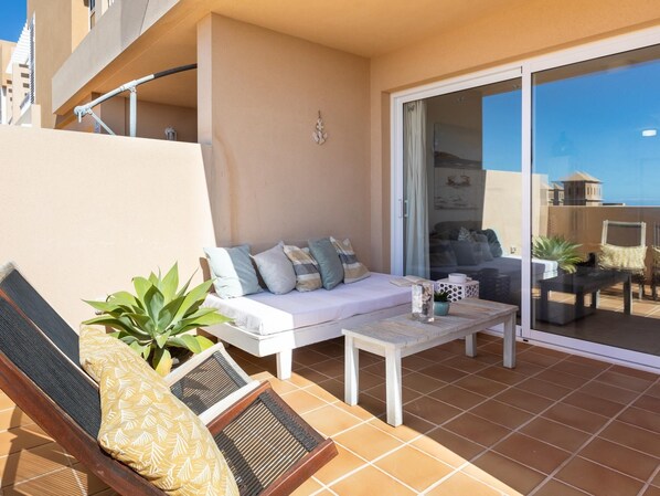 A balcony with a white sofa, a small table, and a chair. There is a potted plant and a decorative item on the table. - Nice terrace apartment, shared pool - PORÍS 2 (Porís de Abona)