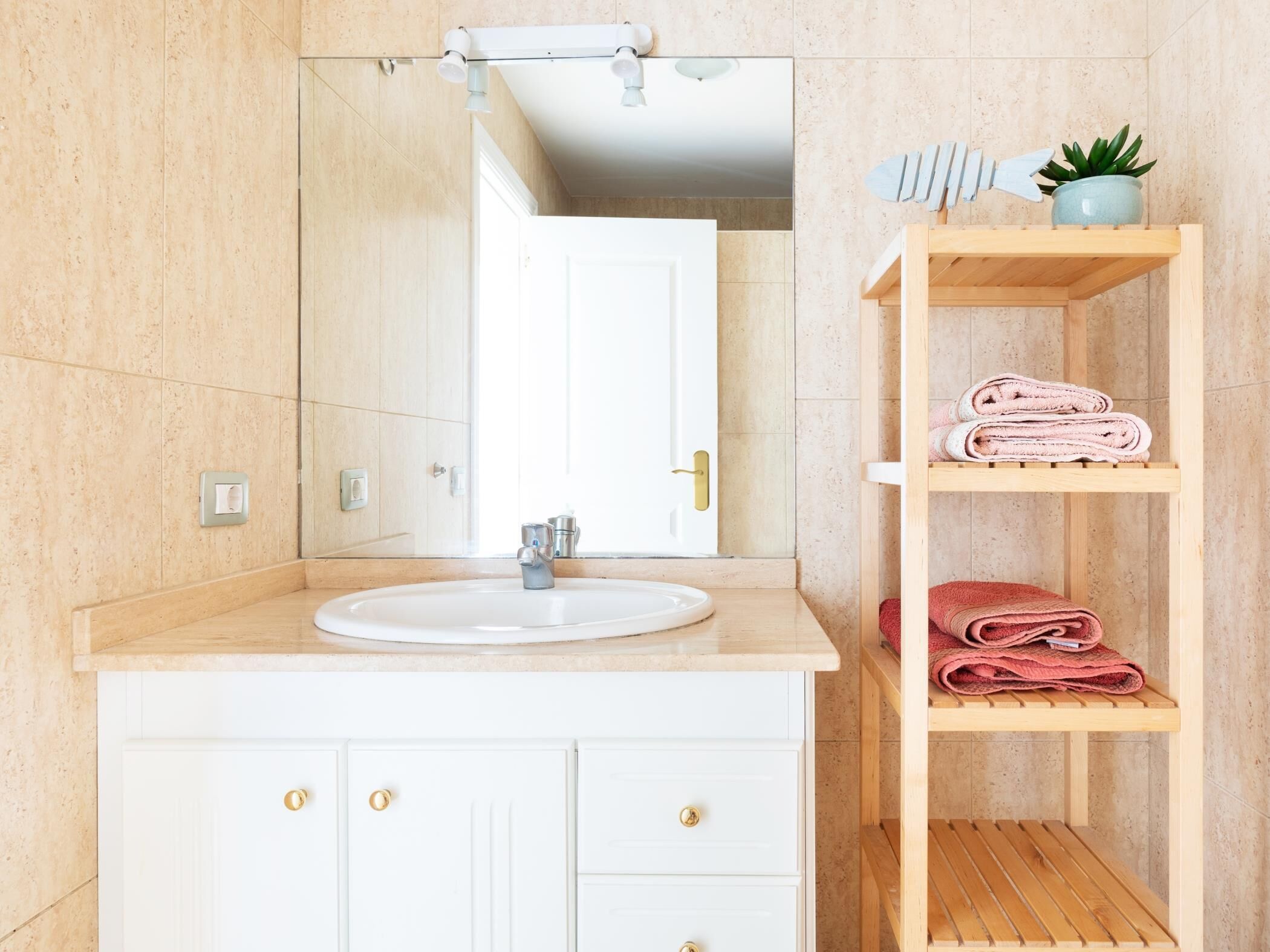 Un baño con un lavabo blanco, tocador de madera y repisas con toallas.