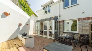 A patio area with a table and chairs, a small seating area, and a door leading to an interior space. - No 4 Pentire Rocks is a contemporary maisonette situated in New Polzeath. (Wadebridge)