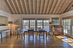 Un comedor con una mesa y sillas de madera, ventanas amplias y techo de madera.