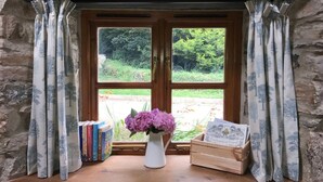 A stone wall with a wooden window framed by curtains, a vase with flowers, and books on a windowsill. - Bwthyn Graig, Llanrhian, Pembrokeshire. Short walk to Porthgain & Beach (Llanrhian)
