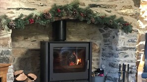 A stone fireplace with a modern wood-burning stove, decorated with Christmas garlands. - Bwthyn Graig, Llanrhian, Pembrokeshire. Short walk to Porthgain & Beach (Llanrhian)