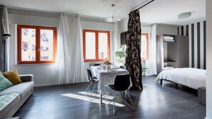 Une chambre d’hôtel moderne comprenant un lit, un coin repas avec une table et des chaises, un canapé et une grande fenêtre avec des rideaux.