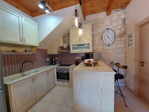 Una cocina con armarios de madera, una pared de piedra, un reloj y una pequeña isla con sillas.