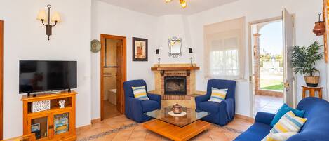 A living room with a television, two armchairs, a sofa, a fireplace, and a door leading to an outdoor area.