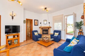 A living room with a television, two armchairs, a sofa, a fireplace, and a door leading to an outdoor area. - Cubo's Casa María los Javieles / free wifi / private pool (Alhaurín el Grande)