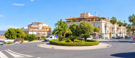 A roundabout with palm trees and a building with a sign that reads 'MUEBLES A GRILLON'.