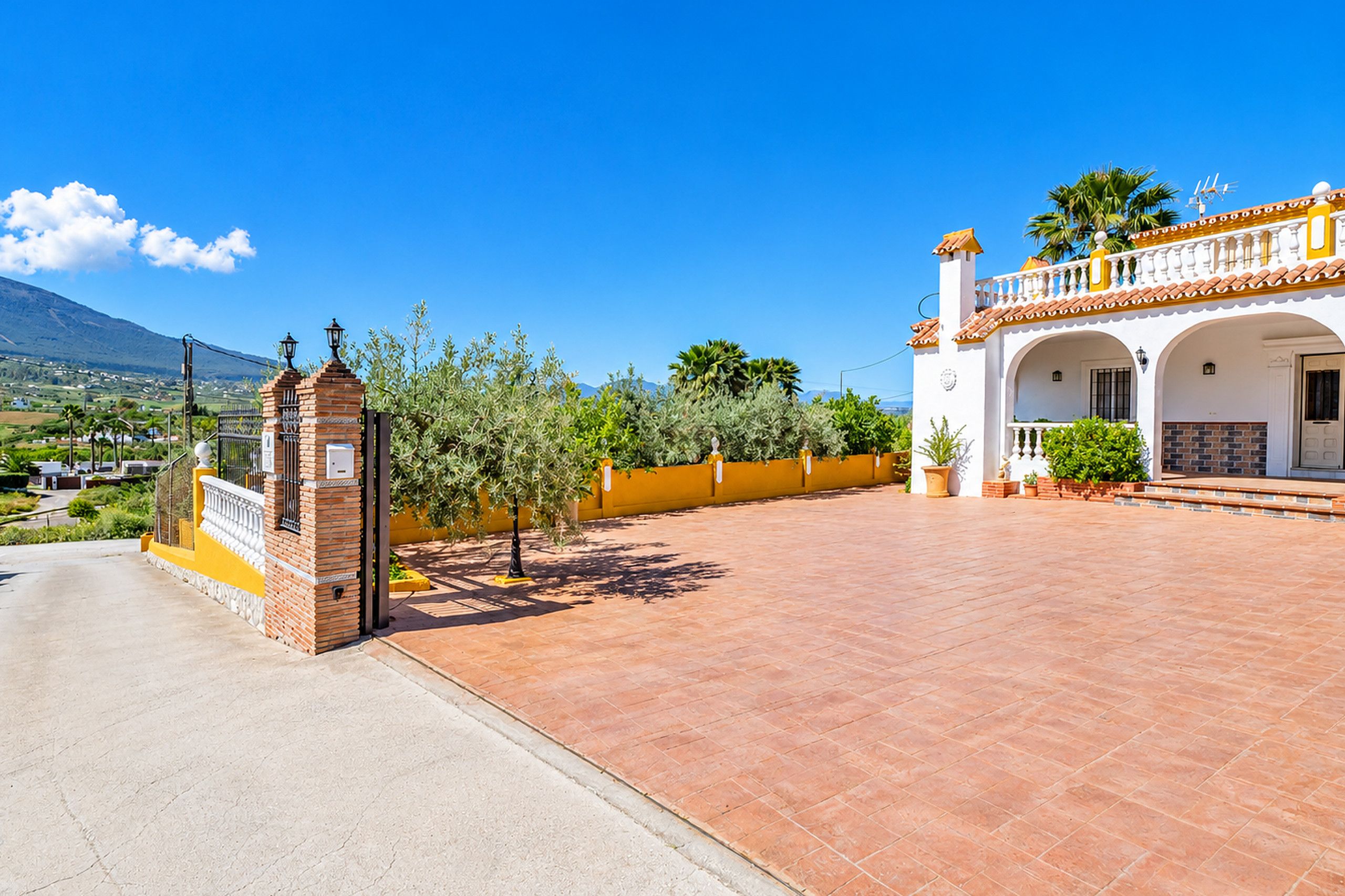 A residential property with a paved courtyard, a brick entrance gate, and a yellow wall.