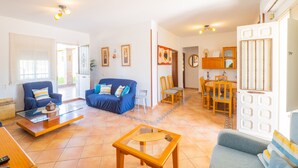 Un salón amplio con un sofá azul, una mesa de centro de vidrio y una zona de comedor con muebles de madera.
