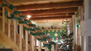 Una escalera de madera adornada con guirnaldas de cintas verdes, un sillón tapizado en verde y un árbol de Navidad en un ambiente de cocina rústica.