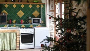 Una cocina rústica con salpicadero de azulejos, vigas de madera, microondas, estufa y un pequeño árbol de Navidad.