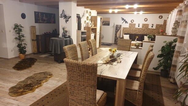 A dining area with a wooden table and wicker chairs, surrounded by potted plants and decorative wall art.
