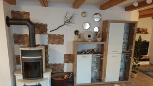 A cozy room with a wood-burning stove, stone wall accents, a glass cabinet with decorative items, and a wooden cabinet with glass doors.