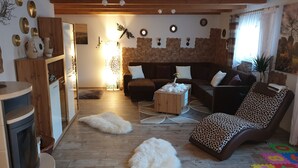 A cozy living room with a fireplace, wooden furniture, a stone wall, and a colorful play mat on the floor.