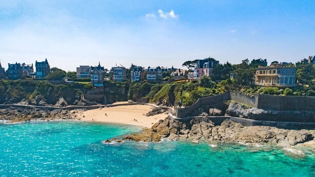 Une ville côtière dotée d’une plage de sable, d’une côte rocheuse et de bâtiments construits le long de la falaise.