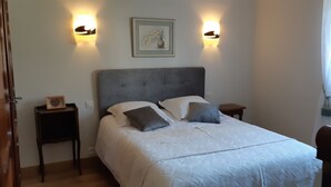 Un lit bien fait, avec une tête de lit grise, deux tables de chevet et des lampes fixées au mur.