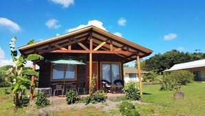 Et lille hus med en træterrasse, et spiseområde med stole og et stort vindue.