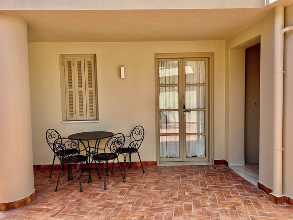 A patio with a table and chairs, a door with a number, and a window with curtains. - Two bedrooms, yard view suite -Themelio suites (Athina)
