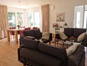 A modern living room with a sofa set, a dining table with chairs, and a kitchen area with a bar.