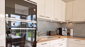 Una cocina moderna con armarios blancos, horno Bosch, cafetera y vistas al exterior.