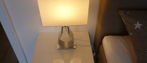A bedside table with a lamp, a drawer, and a bed with a pillow featuring star patterns.