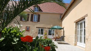 A building with a red-tiled roof, stone walls, and a door with a window. There is a chair and an umbrella outside.