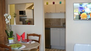 A dining area with a round table, chairs, and a potted plant. There is a kitchen visible in the background with cabinets and a microwave.