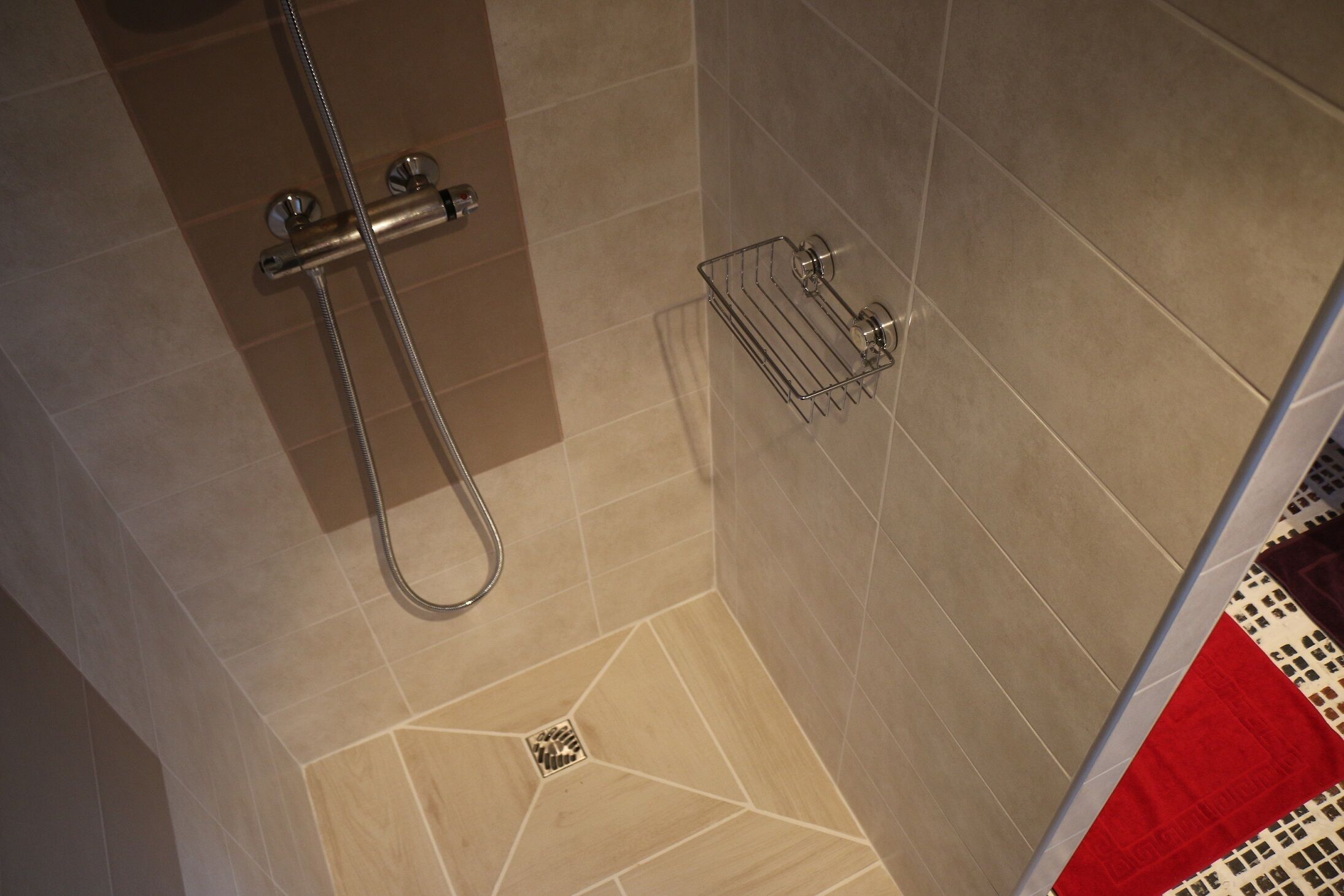 A shower with a metal hose and a metal rack on the wall.