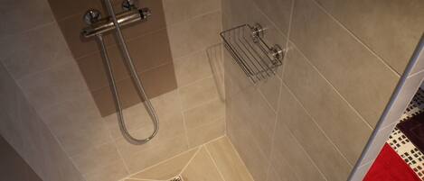 A shower with a metal hose and a metal rack on the wall.