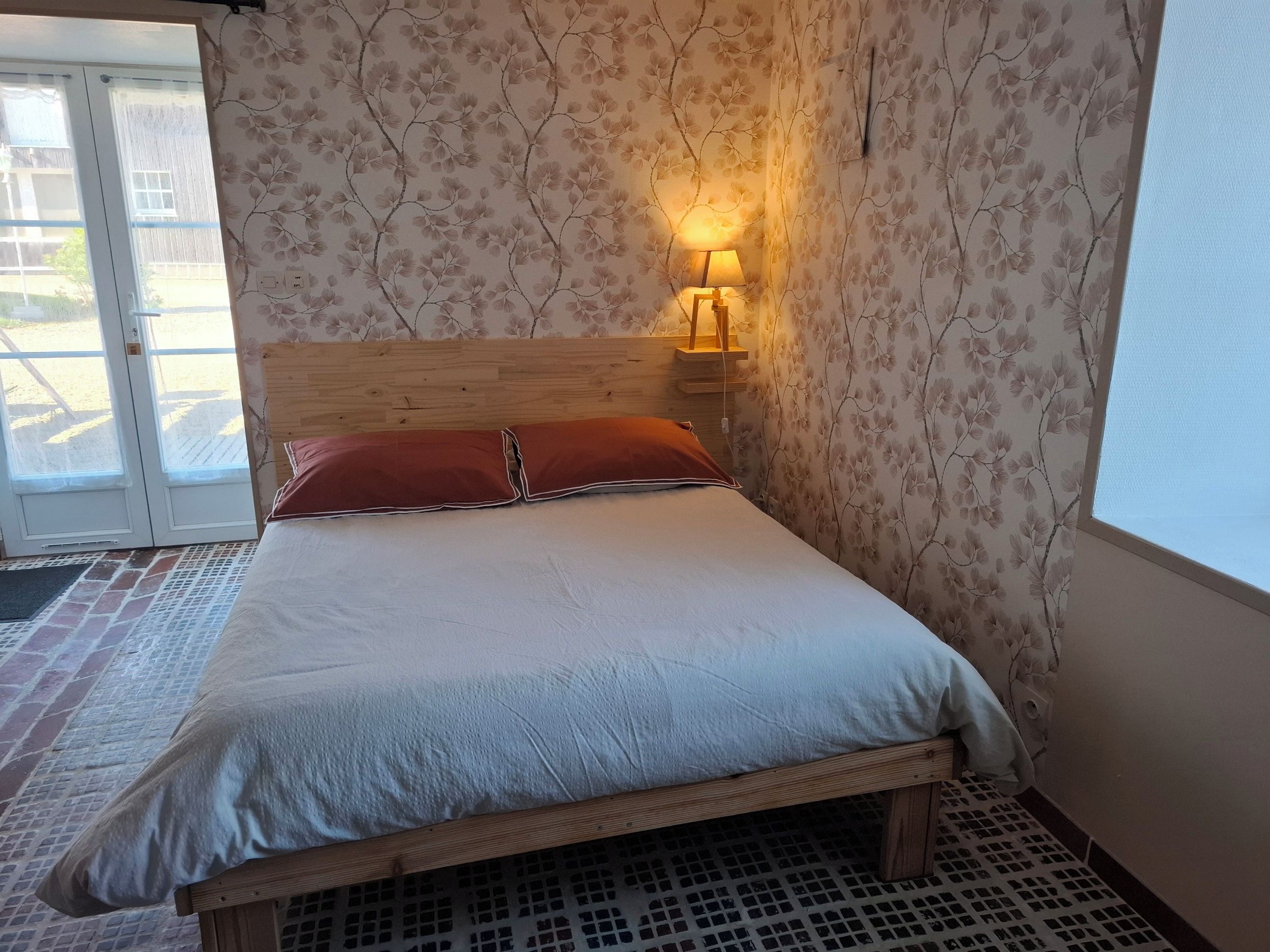 Een kamer met een bed, een wandlamp en een deur die naar buiten leidt.