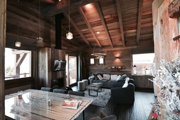 L’intérieur chaleureux d’un chalet avec un plafond en bois, une cheminée, un canapé et un coin repas.