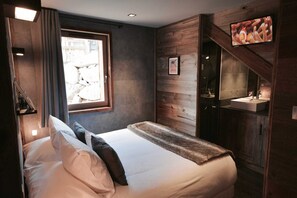A bedroom with a bed, a window, a bathroom with a sink, and a television mounted on the wall.