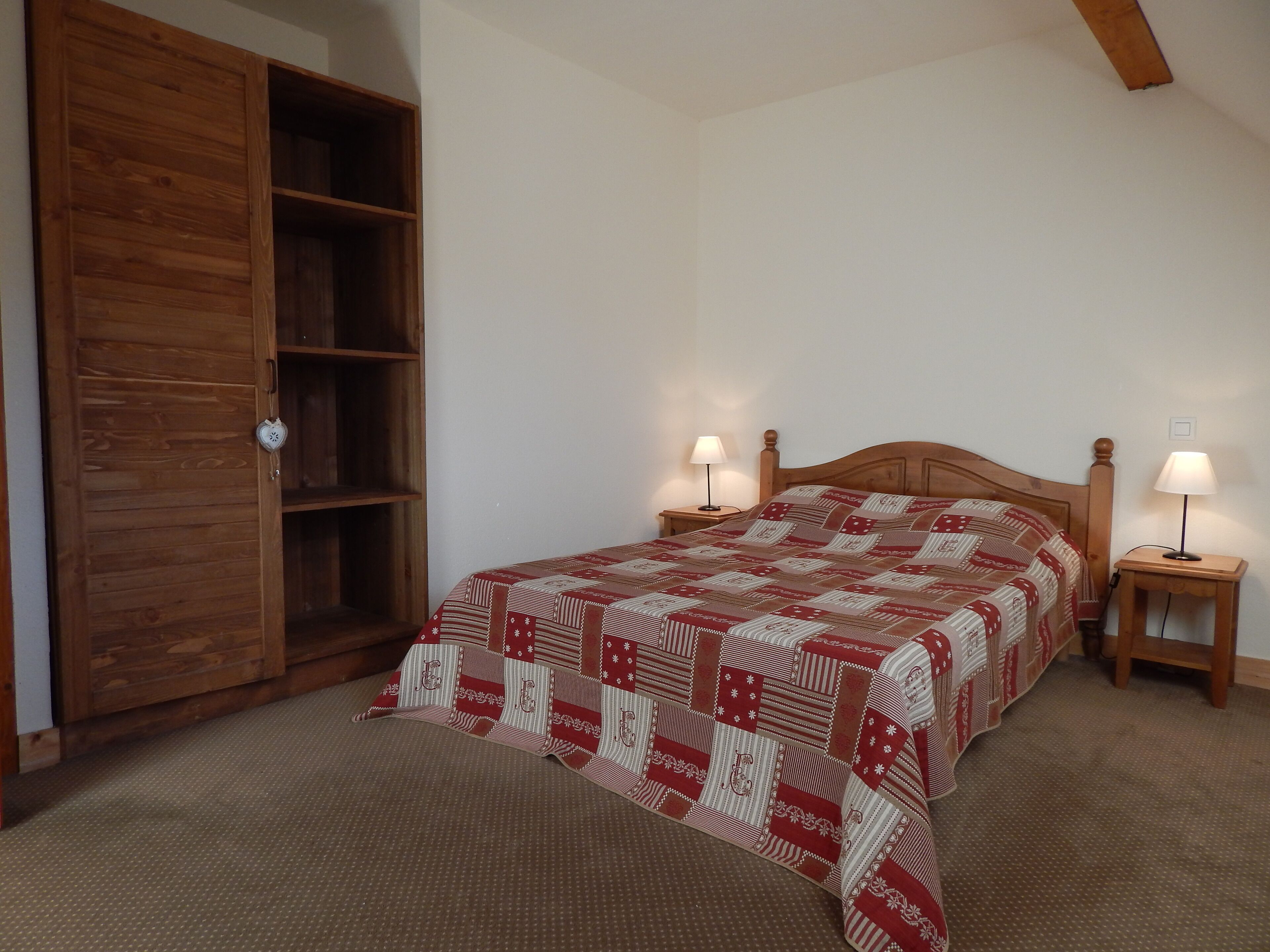 Ein Schlafzimmer mit einem Holzschrank, einem Bett mit gemustertem Überwurf, zwei Nachttischen mit Lampen und einem Teppichboden.