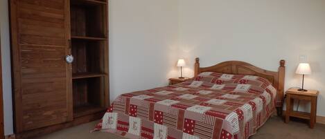 Ein Schlafzimmer mit einem Holzschrank, einem Bett mit gemustertem Überwurf, zwei Nachttischen mit Lampen und einem Teppichboden.