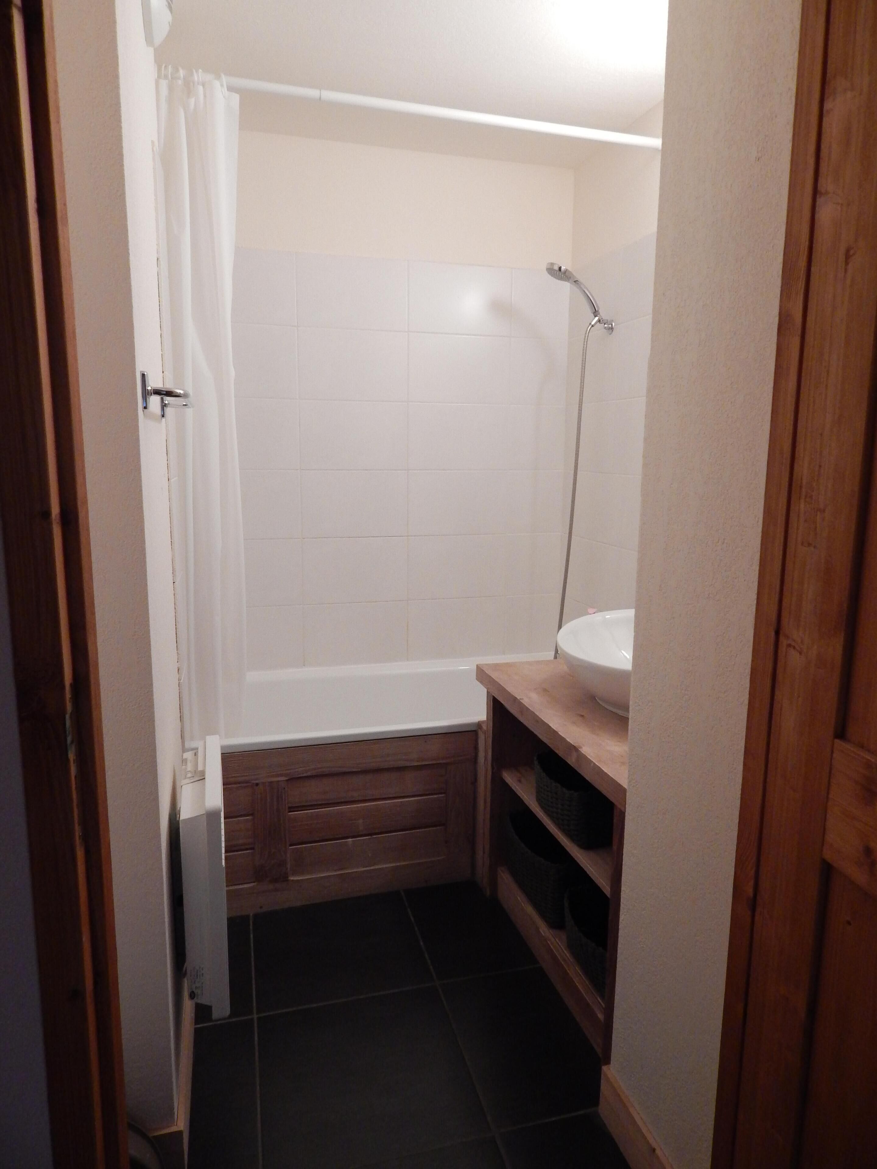 Ein kleines Badezimmer mit einer Badewanne, einem weißen Waschbecken und einem Holzwaschtisch.