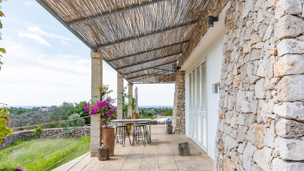 A covered patio with stone walls, a table and chairs, and potted plants. - Hilly Trullo with Sea View (Leuca)