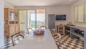 A dining area with a checkered floor, a white table, and chairs. There is a wooden cabinet with glass doors, a television mounted on the wall, and a view through the glass doors. - Hilly Trullo with Sea View (Leuca)